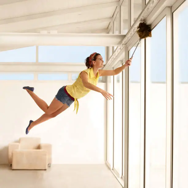 Young woman floating through the air while dusting her house