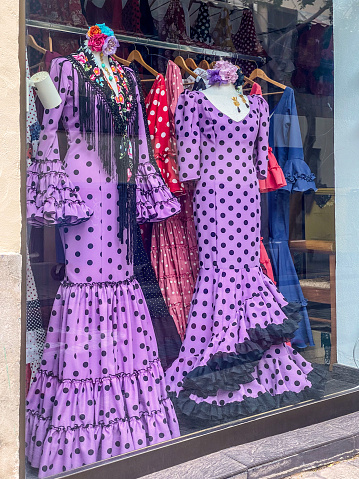 Valencia, Spain - November 12, 2023: Purple flamenco dresses for sale exhibited in store window. This is the dress traditionally worn by women at festivals in the Andalusian Community that became also a Spanish tradition