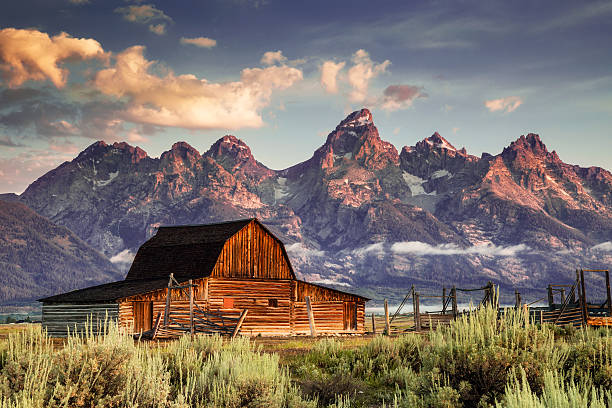 Moulton Barn and Tetons in Morning Light Early morning magenta light illuminates clouds and the Moulton Barn on Mormon Row at the foot of the Grand Tetons near Jackson, Wyoming, USA. ranch stock pictures, royalty-free photos & images
