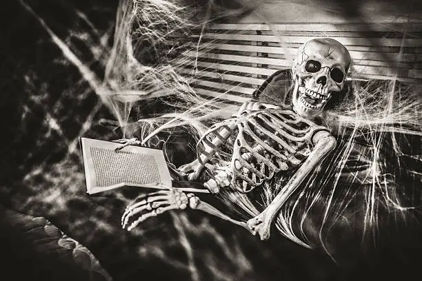 Skeleton reading a novel in bed