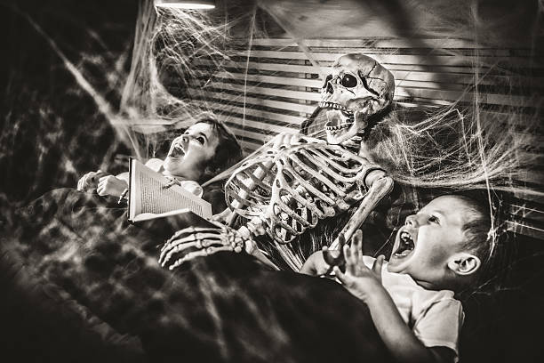 Halloween Bedtime Stories Little girl reading terror stories to her brother and a skeleton. ghost photos stock pictures, royalty-free photos & images
