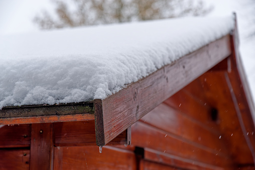 Close-up of wooden shed in a winter with roof covered by white snow
