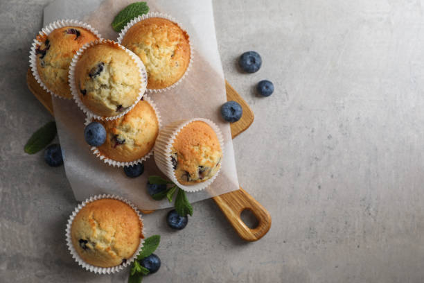 istock Delicious sweet muffins with blueberries and mint on grey table, flat lay. Space for text 1865496552