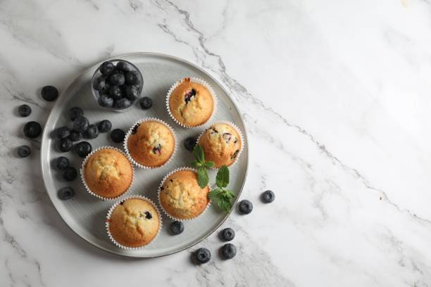 istock Delicious sweet muffins with blueberries and mint on white marble table, flat lay. Space for text 1865497632