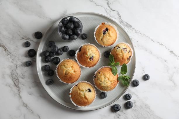 istock Delicious sweet muffins with blueberries and mint on white marble table, flat lay 1865497641