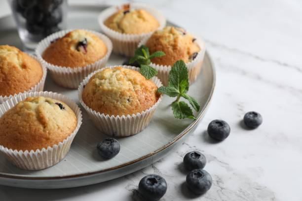 istock Delicious sweet muffins with blueberries and mint on white marble table, closeup. Space for text 1865497643