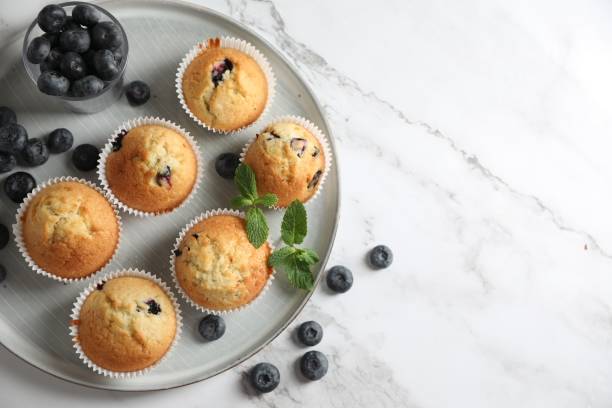istock Delicious sweet muffins with blueberries and mint on white marble table, flat lay. Space for text 1865497644
