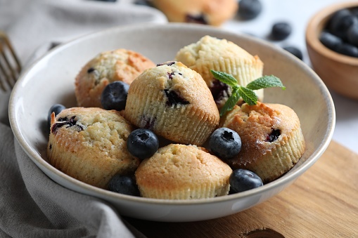 Delicious muffins with blueberries and mint in bowl on table, closeup
