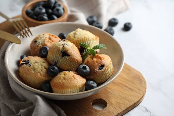istock Delicious muffins with blueberries and mint in bowl on white table, closeup 1865498173