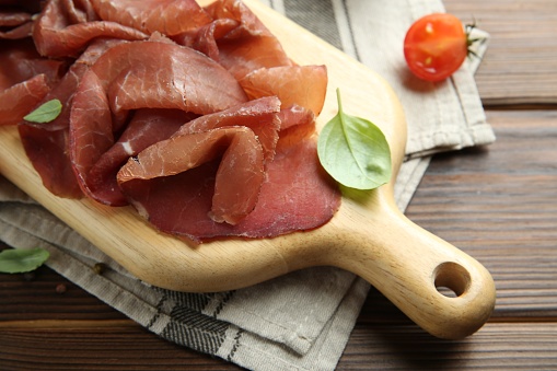 Board with delicious bresaola on wooden table, closeup