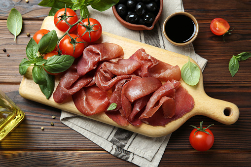 Board with delicious bresaola and other snacks served on wooden table, flat lay