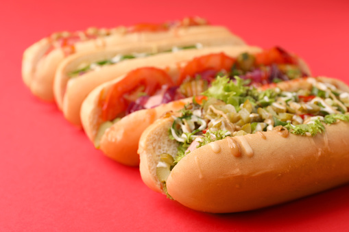 Delicious hot dogs with different toppings on red background, closeup