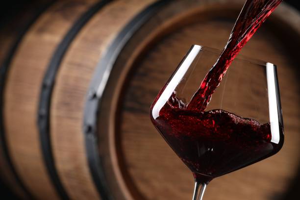 versare vino rosso in vetro vicino a botte di legno, primo piano. spazio per il testo - vino foto e immagini stock