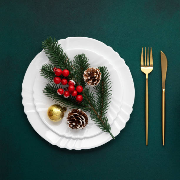 istock Christmas lunch invitation, creative design, art arrangement. Table setting. White plate, golden fork, knife. Pine tree branch on green background. New Year's decorations. Top view. Celebration dinner 1865549692