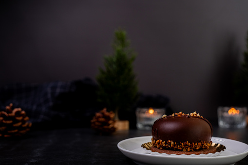 chocolate cake on dark background decorated with candle and plant. Christmas and new year food and pastry.