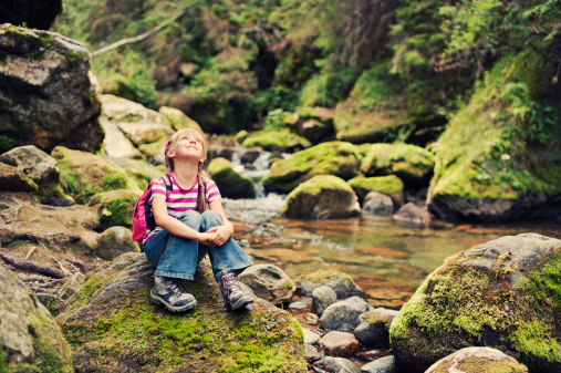 Cute little girl resting by the beautiful mountain stream.