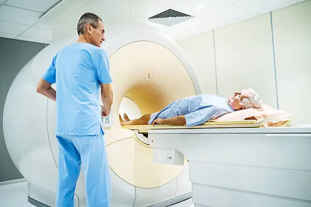 Senior man entering into the MRI Scanner, while mature radiologist is pressing the start button.  
