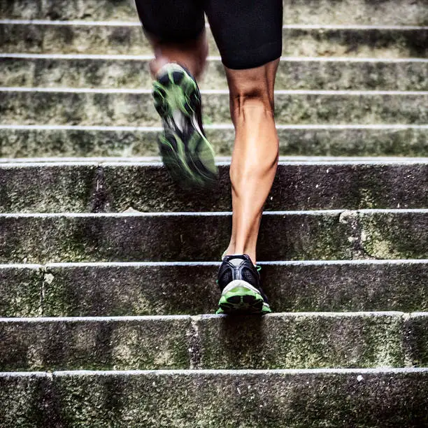 Close up of man with muscular legs running up a flight of stairs in old European city.