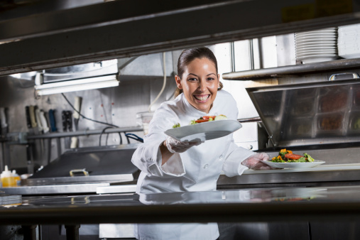 Female Hispanic chef (30s) in commercial kitchen, preparing gourmet salad.