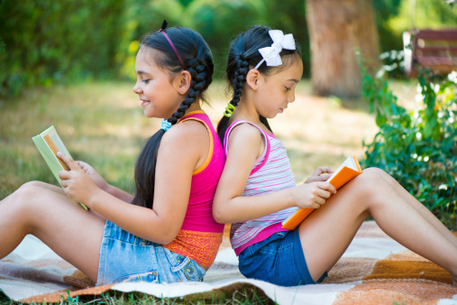 Hispanic sisters reading book in summer park