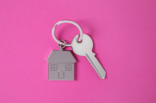 Key with keychain in shape of house on pink background, top view