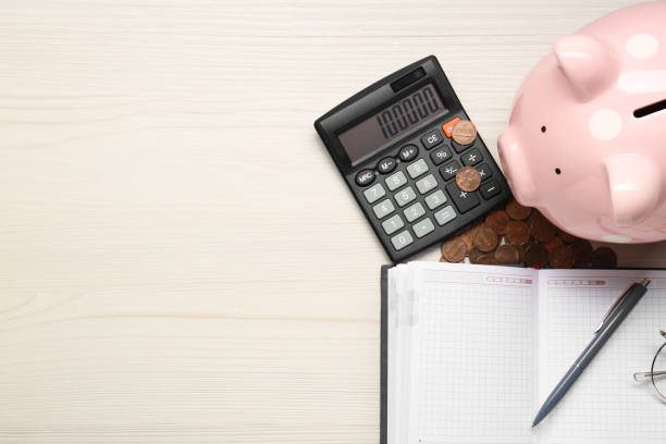 istock Calculator, piggy bank, notebook and coins on white wooden table, flat lay. Space for text 1865586462