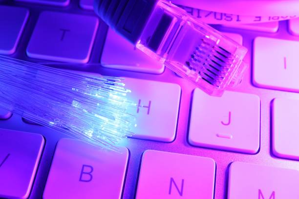 istock Optical fiber strands transmitting color light near cable with modular connector on computer keyboard, closeup 1865588770