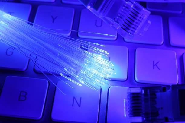istock Optical fiber strands transmitting color light and modular connectors on computer keyboard, closeup 1865588783