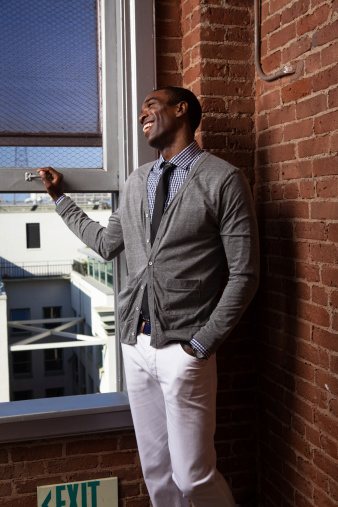 A smiling young African-American urbanite looking out the window of an upper-floor loft apartment.