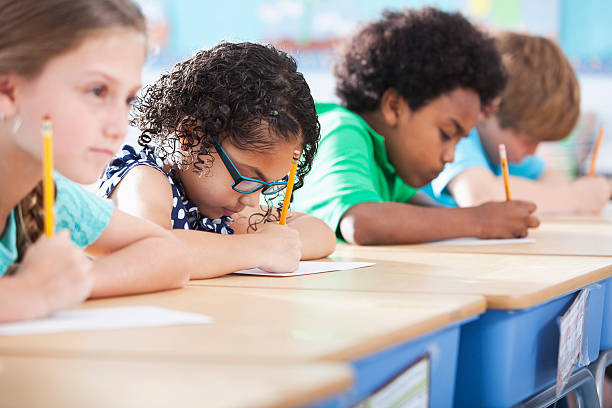 Elementary school children writing in class Multi-ethnic elementary school children writing in classroom.  Focus on Hispanic girl wearing eyeglasses (8-9 years). primary school exams stock pictures, royalty-free photos & images