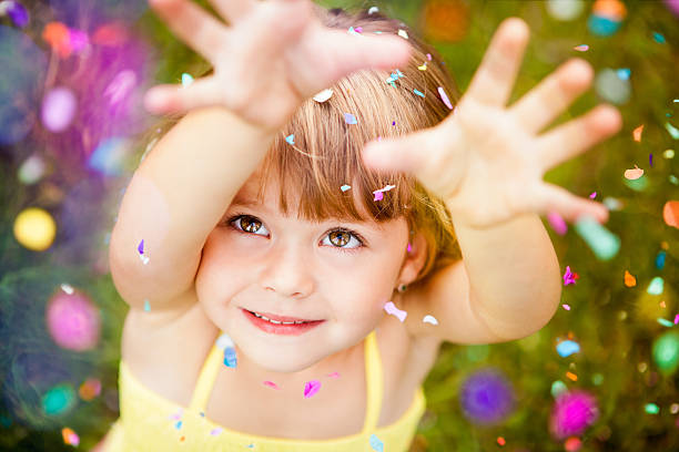 Confetti Falling On Little Girl Portrait Of A Happy Little Girl Looking Up At Confetti Falling On Her hand raised photos stock pictures, royalty-free photos & images