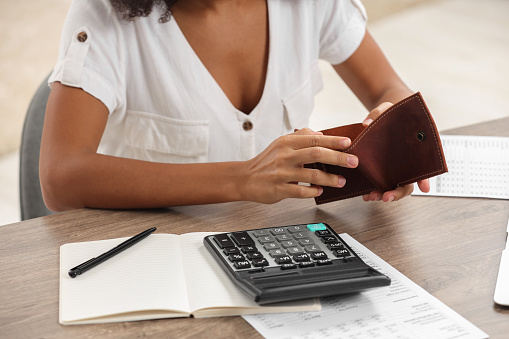 Woman with empty wallet and calculator planning budget at table indoors, closeup. Debt problem