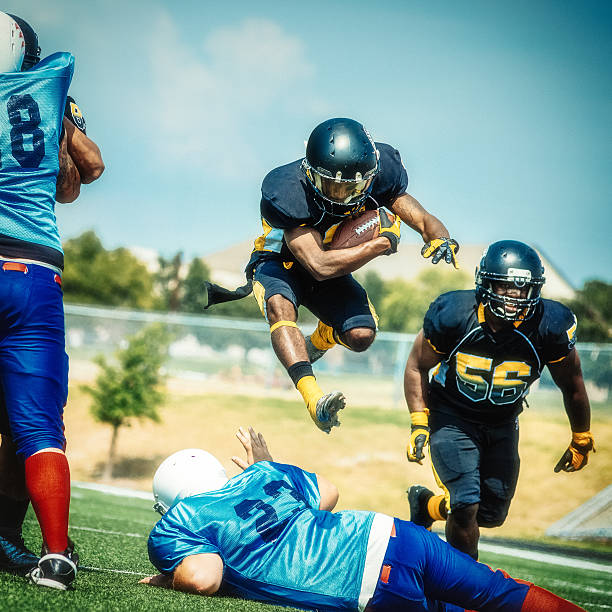 Two American football players in action. One of the players is overflying the other and scoring the touchdown.   
