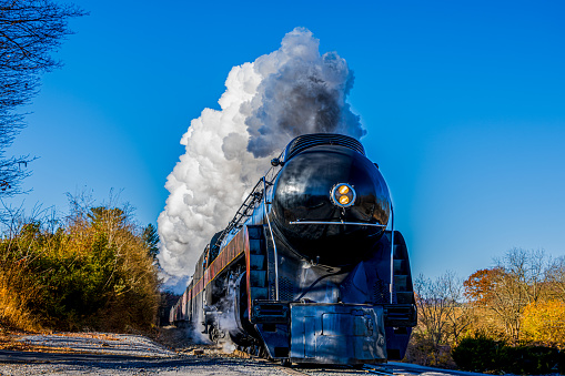 A picture of a black steam train moving on a rail track with smoke coming out of the chimney the picture is taken high above looking down