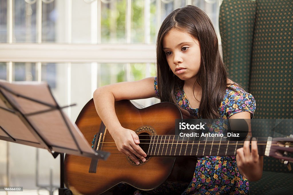 Learning how to play the guitar Pretty little brunette reading a sheet music and playing the guitar Beautiful People Stock Photo