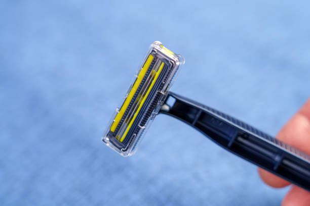 istock Disposable blue razor with steel sharp blades in hand on a jeans background. 1865661457