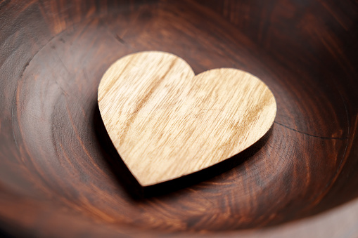 One carved wooden heart in brown rustic bowl close up. Romantic love concept.