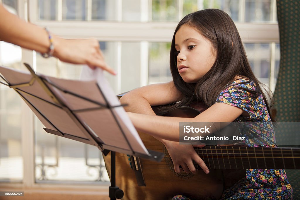 Taking guitar lessons Cute little girl playing the guitar during one of her guitar lessons at home Beautiful People Stock Photo