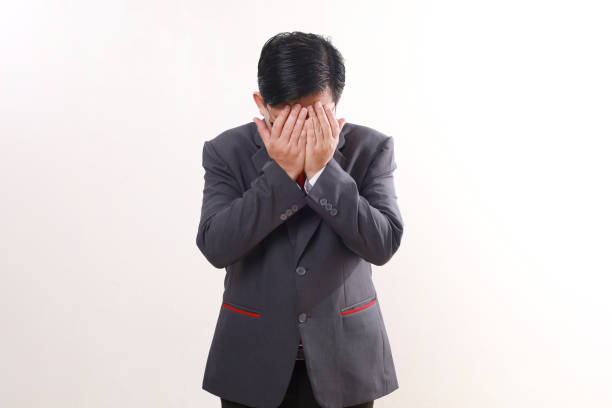 istock Stressed asian businessman standing while covering face. Isolated on white background 1865670857