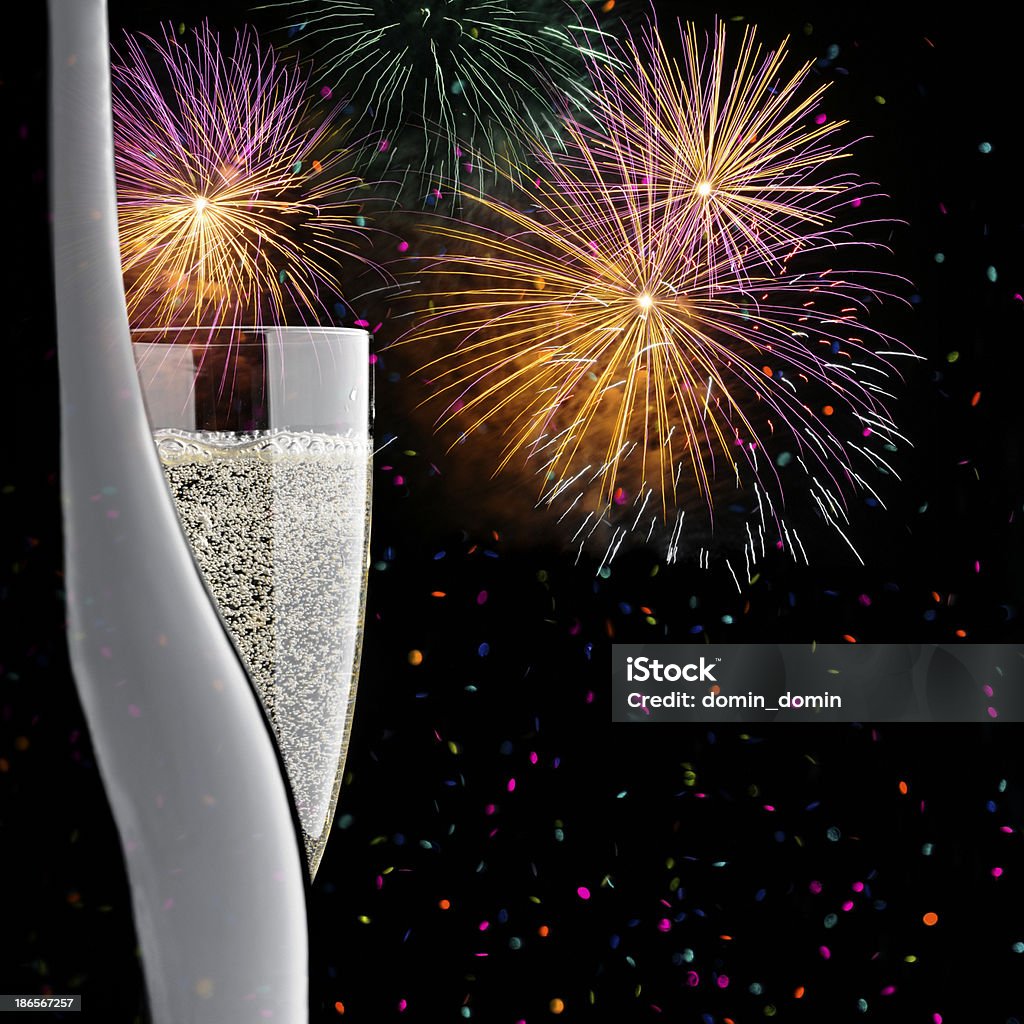 Close-up of glass and bottle of Champagne, confetti, fireworks display Glass and bottle of Champagne, falling confetti, against multicolored fireworks display, night, black background. Alcohol - Drink Stock Photo