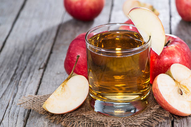 Glass of apple cider surrounded by freshly-cut apples Apple Juice with fresh fruits on wooden background apple juice photos stock pictures, royalty-free photos & images