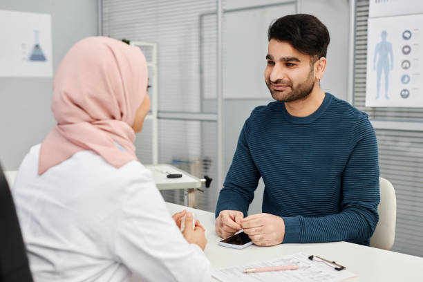 Patient Visiting Doctor in Hospital Medium shot of smiling male Muslim patient listening to female doctor wearing headscarf during consultation in clinic wafid medical appointment = stock pictures, royalty-free photos & images