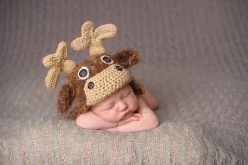 A newborn sleeping in a moose knit hat.