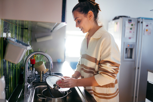 Young beautiful woman washing the dishes in her kitchen