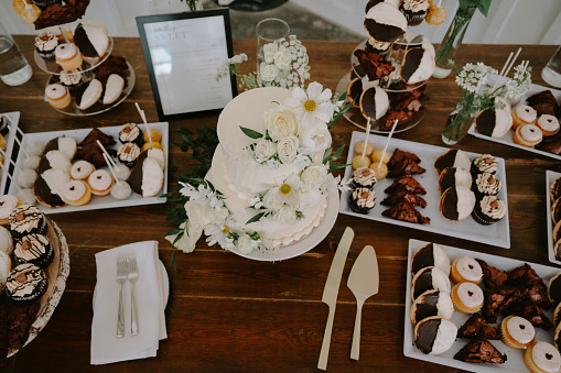 Luxurious desert table with tired white cake with flower, decorated cookies, and cupcakes. Neutral tones