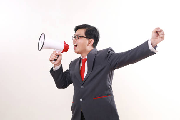 istock Asian businessman celebrating victory using megaphone while clenching hand. Isolated on white 1865731082