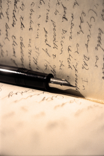 A black and silver fountain pen rests between the pages of a man's journal. This sepia-toned photograph was shot on high ISO film and has a noticeable grain pattern and retro feel.