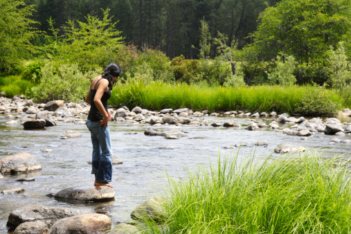 Beautiful young hispanic woman standing in mountain river.