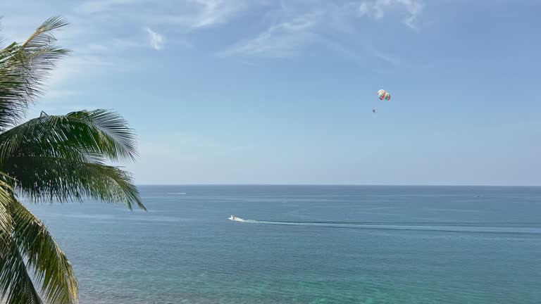 The coast of Thailand on a sunny day, beach entertainment - parachute behind a motorboat, people parachute over the sea