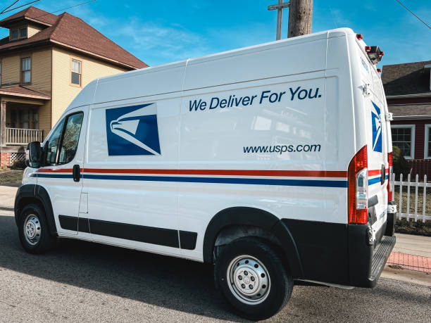 Fort Lauderdale, Florida, USA - September 3, 2020:  Mailman delivering mail in a postal truck puts letters into a red mailbox.